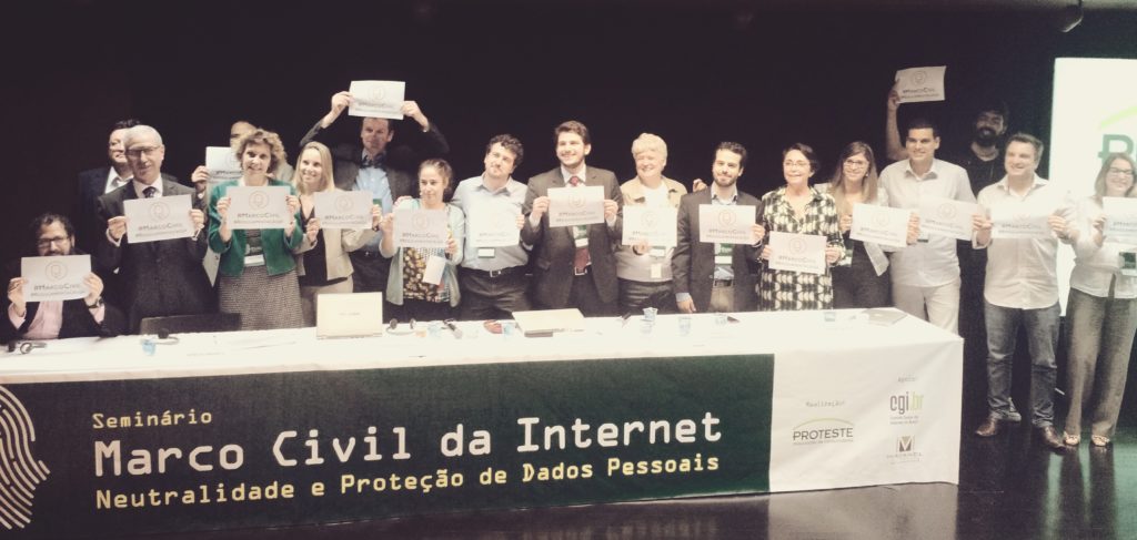 Photo of 18 people standing, holding a paper, behind a bench that says: "Seminar: Civil Rights Framework for Internet Neutrality and Personal Data Protection".
